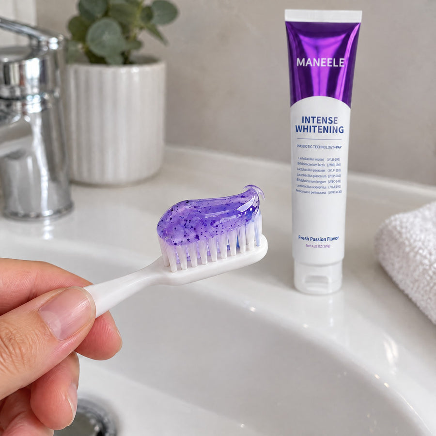 Hand holding a toothbrush topped with purple gel toothpaste over a white sink, the Maneele tube behind it